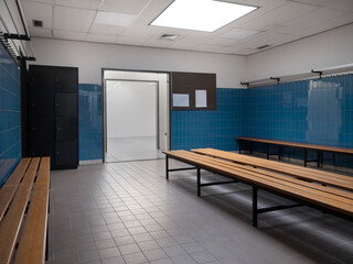 Sports hall locker room interior with metal lockers wooden benches and blue tiled walls with open doorway