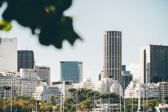 Modern skyline of Rio de Janeiro with tall office buildings, palm trees and marina in foreground under clear blue sky, showcasing urban architecture and tropical city atmosphere