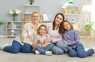 Portrait of a happy family with grandmother, mother, and two children sitting together on the floor at home living room, showcasing love and affection, bonding and warm relationship dynamics.