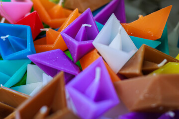 Close-up of a basket filled with colorful origami boat-shaped candles in vibrant hues of purple,...