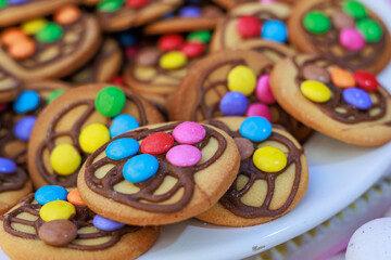Close-up of a white plate filled with homemade cookies decorated with colorful candy-coated chocolates and chocolate drizzle, creating a fun and festive dessert presentation