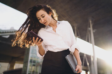 Focused freelancer with smartphone and tablet, standing outdoors, representing independence, modern...