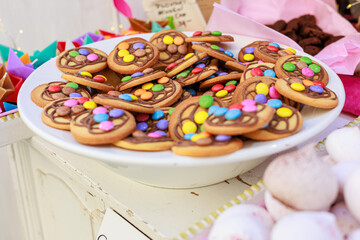 Close-up of a white plate filled with homemade cookies decorated with colorful candy-coated chocolates and chocolate drizzle, creating a fun and festive dessert presentation