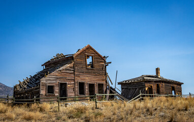 Image of a dilapidated building and fence on a grassy hill on a sunny day with a bright blue sky.