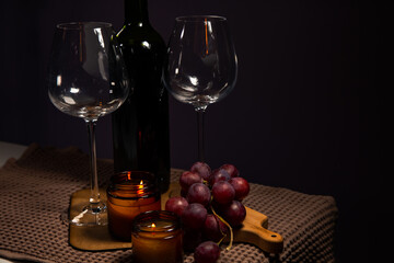 Still life two wine glasses with grapes bunch near romantic aroma burning flame fire candles on a table on dark backround. Decor concept of Christmas holiday celebration with fresh sweet ripe dessert
