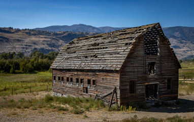 Scenic view of a dilapidated old wooden barn in a valley with mountains in the distance.