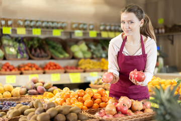 Young woman seller in apron puts fresh pomegranate on display at vegetable market