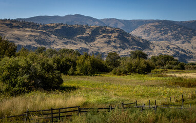 Scenic view of a pasture in a valley with a wooden fence in the foreground and mountains in the background.