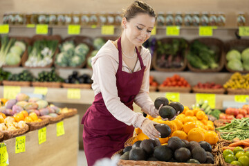 Young woman seller in an apron lays out a soft avocado on the counter of a vegetable shop. Delicious avocado for a healthy breakfast