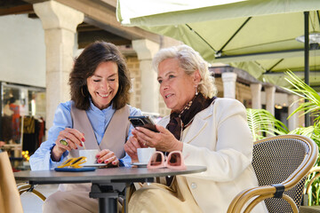 Happy Senior women friends relaxing and using smartphone in cafe
