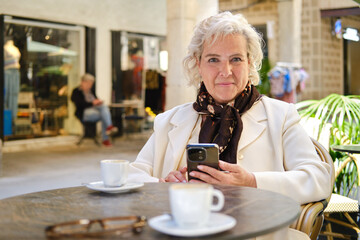 confident Senior woman enjoying coffee looking at camera  resting on a cafe in Barcelona street