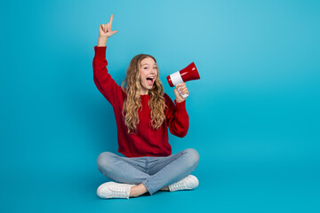 Adorable young woman holding a red megaphone, dressed in casual style with a red sweater, sitting...