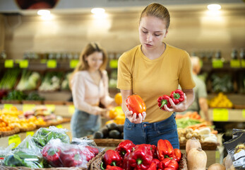 Girl selects ripe bell peppers from counter in a grocery store