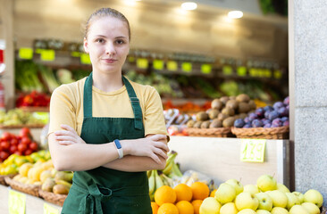 Young woman seller in apron posing at vegetable market