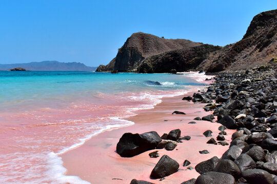 Pink beach with clear turquoise water, black boulders, near Komodo Island, Indonesia