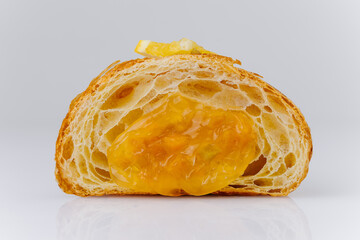 Fresh croissant with orange filling and candied slices on white background, gourmet pastry