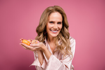 Smiling mature woman holding colorful decorative eggs against pink background, showcasing happiness and gentle beauty