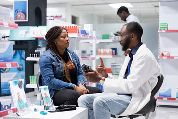 Obraz premium Professional black pharmacist providing expert medication advice to a female customer at the drugstore, explaining dosage and treatment options during a routine consultation service.