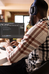 Male software developer with headphones coding from home, using computer to review programming...