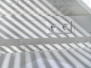 European power sockets with striking striped shadow pattern cast by window covering on white wall