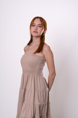 Fototapeta premium Red-haired woman posing with arms back and confident look, beige dress studio portrait.
