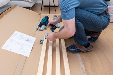 A Caucasian man using a cordless drill, assembling furniture.