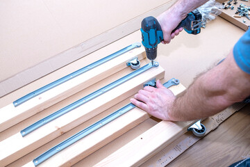 Close-up of a man's hands working with a cordless drill, assembling furniture.