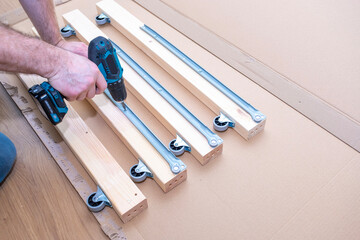 Close-up of a man's hands working with a cordless drill, assembling furniture.