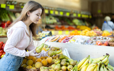 Young woman buyer choosing fresh pears at vegetable market