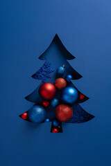 A vertical stylized blue Christmas tree cutout with red and blue ornaments creates a festive...