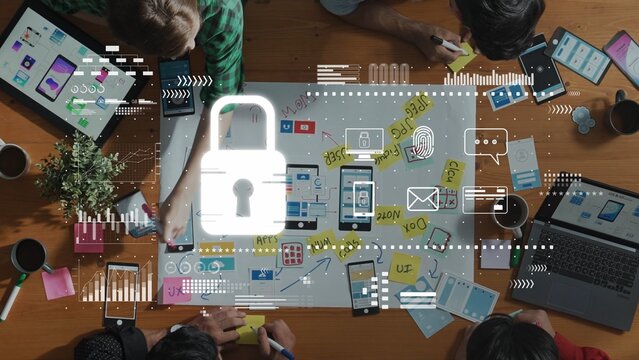 A diverse team collaborates in a modern office, brainstorming cybersecurity concepts while using digital devices and creating visual plans on a wooden table. Raster