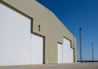 Wide beige hangars with closed white segmented doors and number markings at military airbase