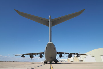 Tactical transport aircraft seen from behind showing tail structure and engines under clear sky