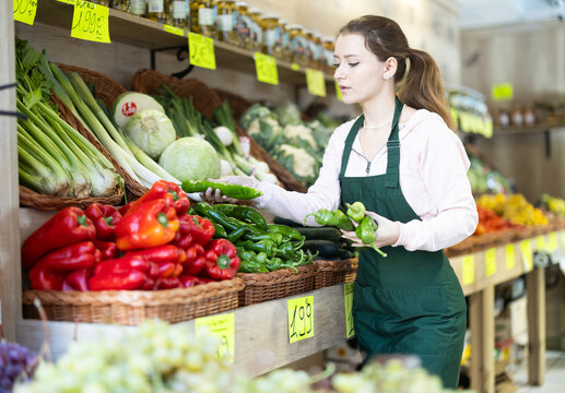Girl employees in uniform holding fresh bell pepper in grocery shop - Powered by Adobe