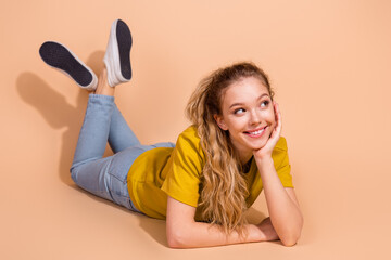 Smiling young woman lying on beige background wearing casual clothes, relaxed and cheerful pose