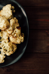 Roasted cauliflower served on a black plate on wooden table