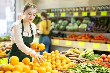 Portrait of girl working in grocery shop as job experience, selling ripe oranges