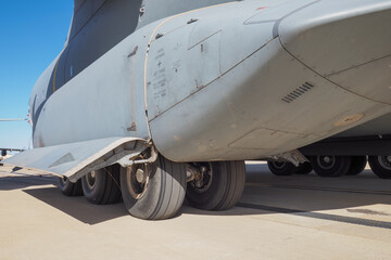 Detailed view of main landing gear and lower fuselage of tactical airlifter on runway surface