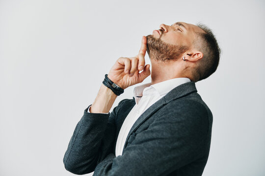 A professional man in a suit stands against an isolated color background, exuding focus and confidence as he thoughtfully rests a finger near his lips, ready to make a strategic decision.