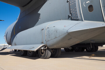 Close-up of large multi-wheel landing gear under tactical airlifter fuselage on runway