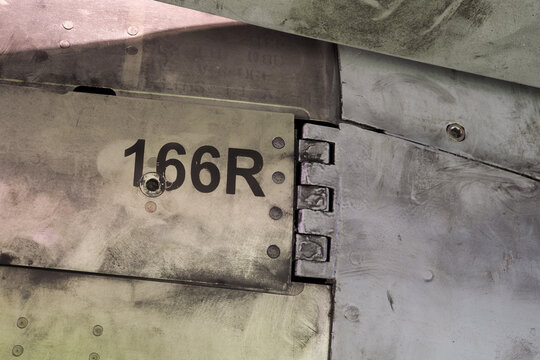 Close view of metallic aircraft panel hinge with number marking and visible fasteners on a multirole fighter jet airframe