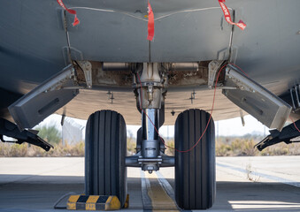 View of the aircraft front landing gear with open bay panels and red safety remove-before-flight tags visible on the ramp
