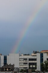 A vibrant rainbow graces the cloudy sky above city rooftops, bringing color and light to an urban afternoon.