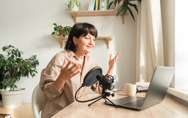Mature caucasian female podcaster engaging in online discussion with laptop and microphone setup