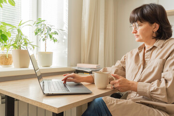 Woman working with laptop from home, drinking coffee
