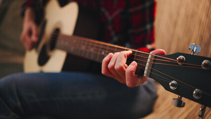 Fingers glide over guitar strings in a relaxed home atmosphere, creating music while seated on a comfortable couch in evening light. © Марина
