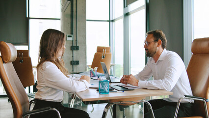 Obraz premium Business meeting between colleagues make a deal and shake hands in a modern office setting during the day discussing project details and strategies with laptops and documents