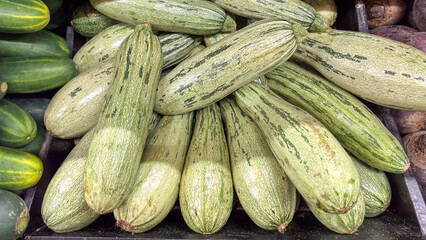 Close-up of bulk cylindrical zucchini squash (Cucurbita pepo). Light green vegetables with dark stripes, displayed for sale at a market or fair.