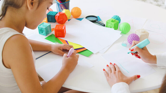 Child engages in creative drawing alphabet with a speech therapist in a bright therapy room focusing on communication skills development