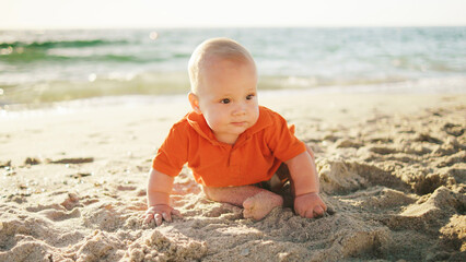 Baby explores the sandy beach during a sunny day by the sea, enjoying the warmth and texture of the sand while gazing ahead